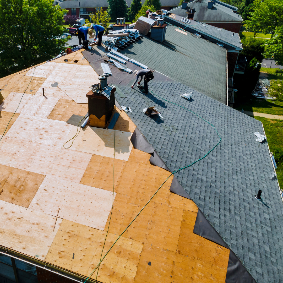 Aerial drone view of a Supreme Restorations crew installing new asphalt shingles on a Maryland residential roof with exposed sheathing visible during mid-replacement
